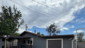 Garagem residencial com calçada de concreto, varanda coberta e gramado.