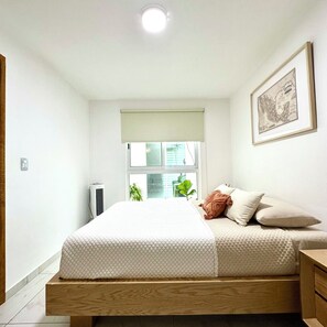 A bedroom with a bed, a bedside table, a window with a view, a radiator, and a framed map on the wall. - Casa Legaspi, Perfect for Work and Relaxation in GDL (Guadalajara)