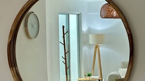 Un mirall rodó amb marc de fusta que reflecteix una habitació amb taula blanca, cadires, una làmpada i una finestra.