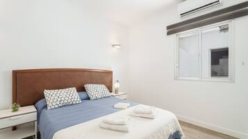 Ein modernes Schlafzimmer mit einem Holzkopfteil, einem Nachttisch mit Lampe, einem Fenster mit Blick und ordentlich gefalteten Handtüchern auf dem Bett.