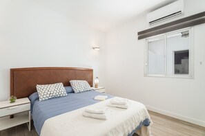 Ein modernes Schlafzimmer mit einem Holzkopfteil, einem Nachttisch mit Lampe, einem Fenster mit Blick und ordentlich gefalteten Handtüchern auf dem Bett.