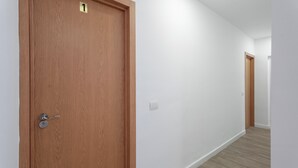 Un pasillo con una puerta de madera marcada con el número 1, un interruptor de luz y otra puerta al final.