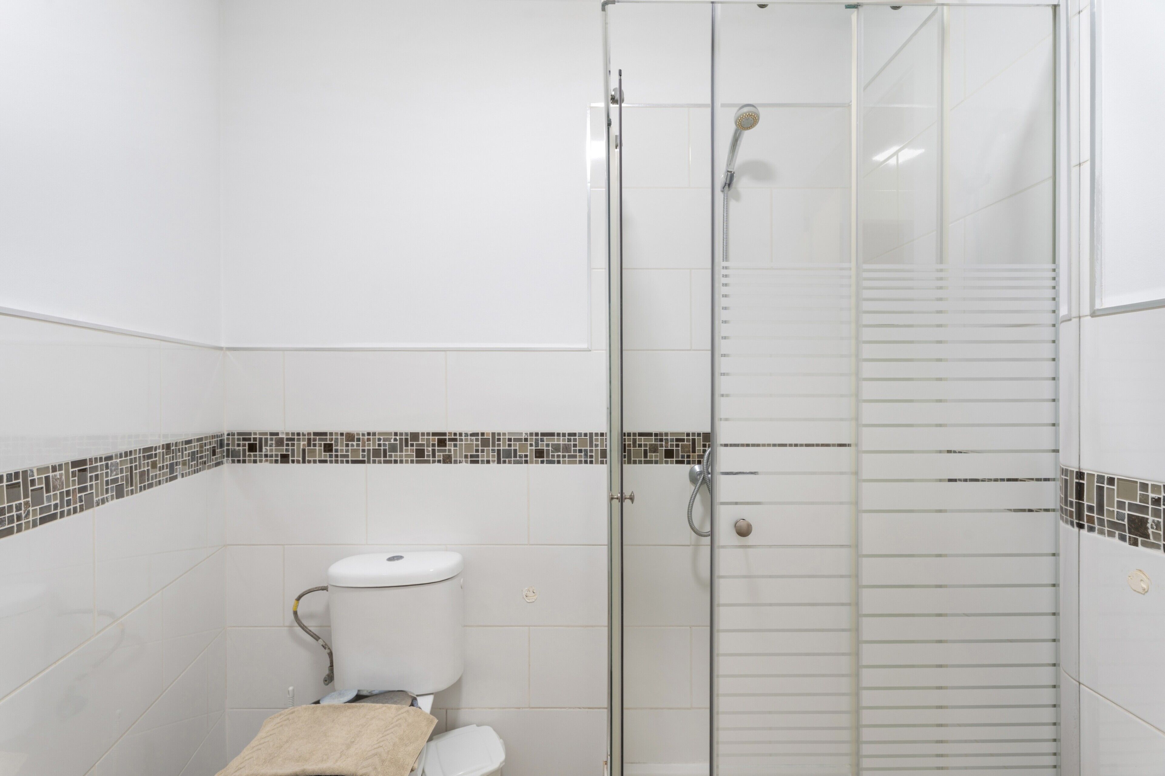 A bathroom with a toilet, a shower enclosure, and a tiled floor.