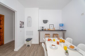 Een moderne eetruimte met een witte tafel gedekt voor het ontbijt, inclusief croissants, fruit en sap.