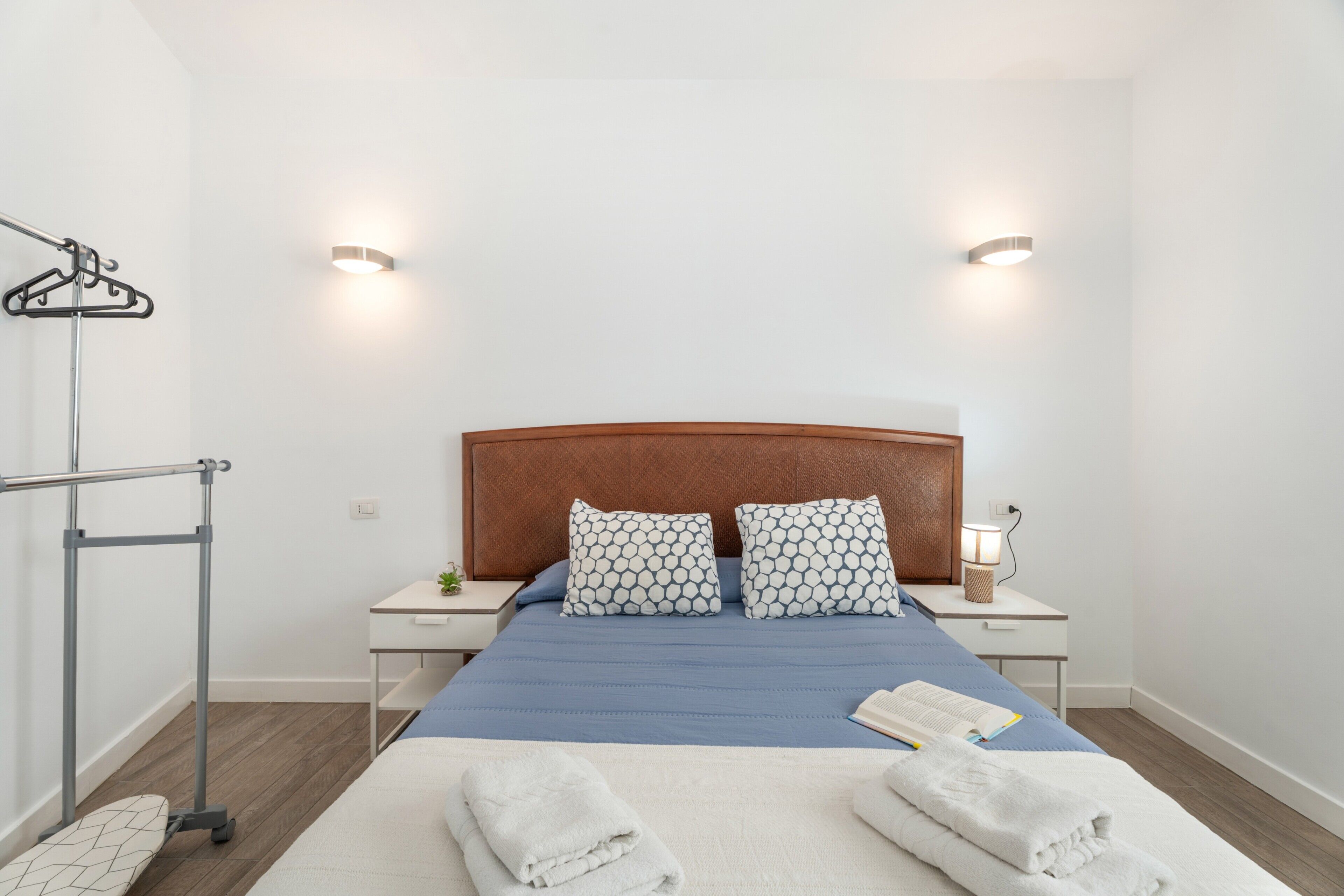 Une chambre d’hôtel comprenant un lit, deux tables de chevet, une petite table, une lampe fixée au mur et un porte-serviettes.