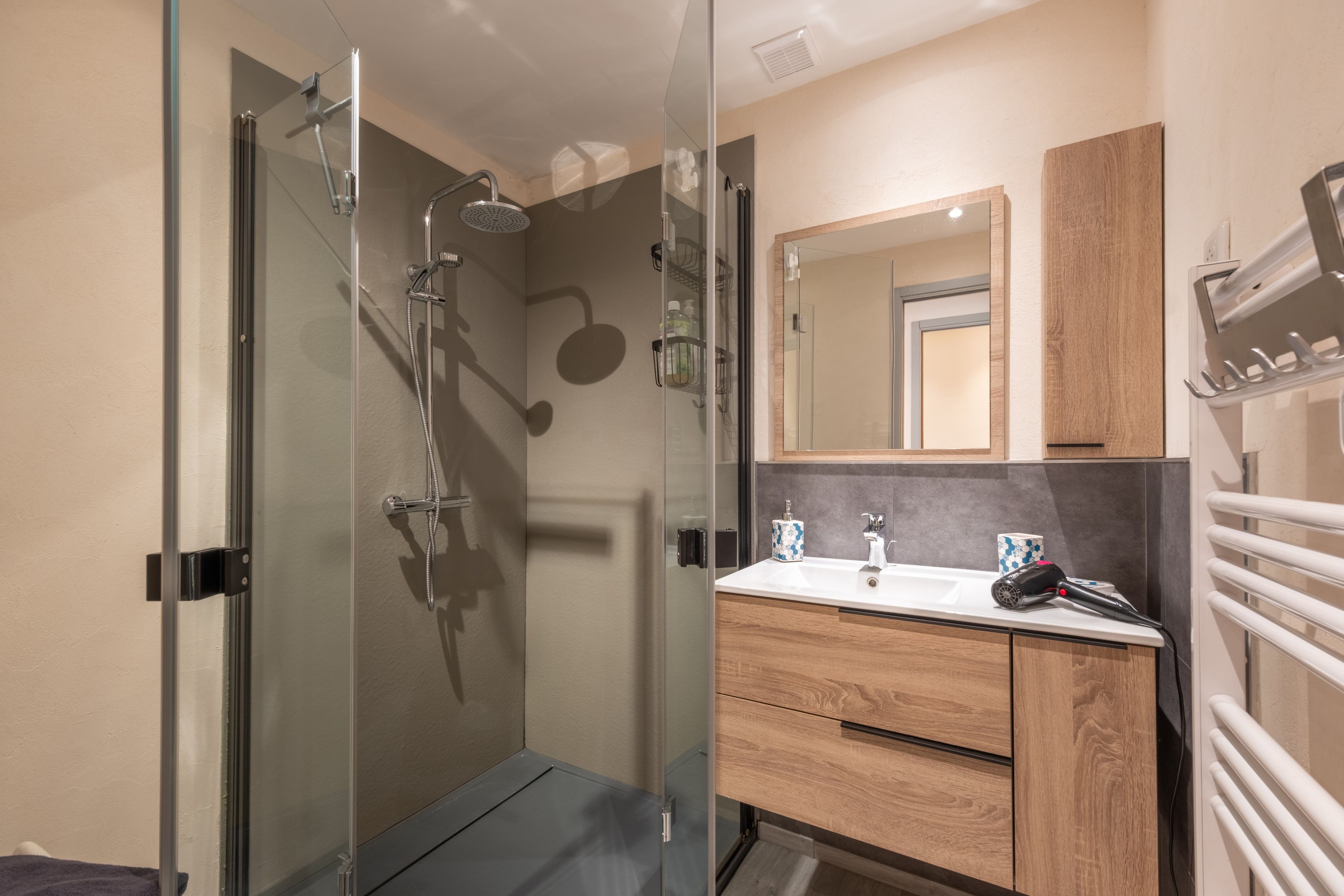 A modern bathroom with a glass shower enclosure, a wooden vanity, and a mirror above the sink.