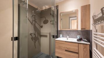 A modern bathroom with a glass shower enclosure, a wooden vanity, and a mirror above the sink.