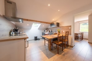 A modern kitchen with a dining area, wooden flooring, and a large window providing natural light.