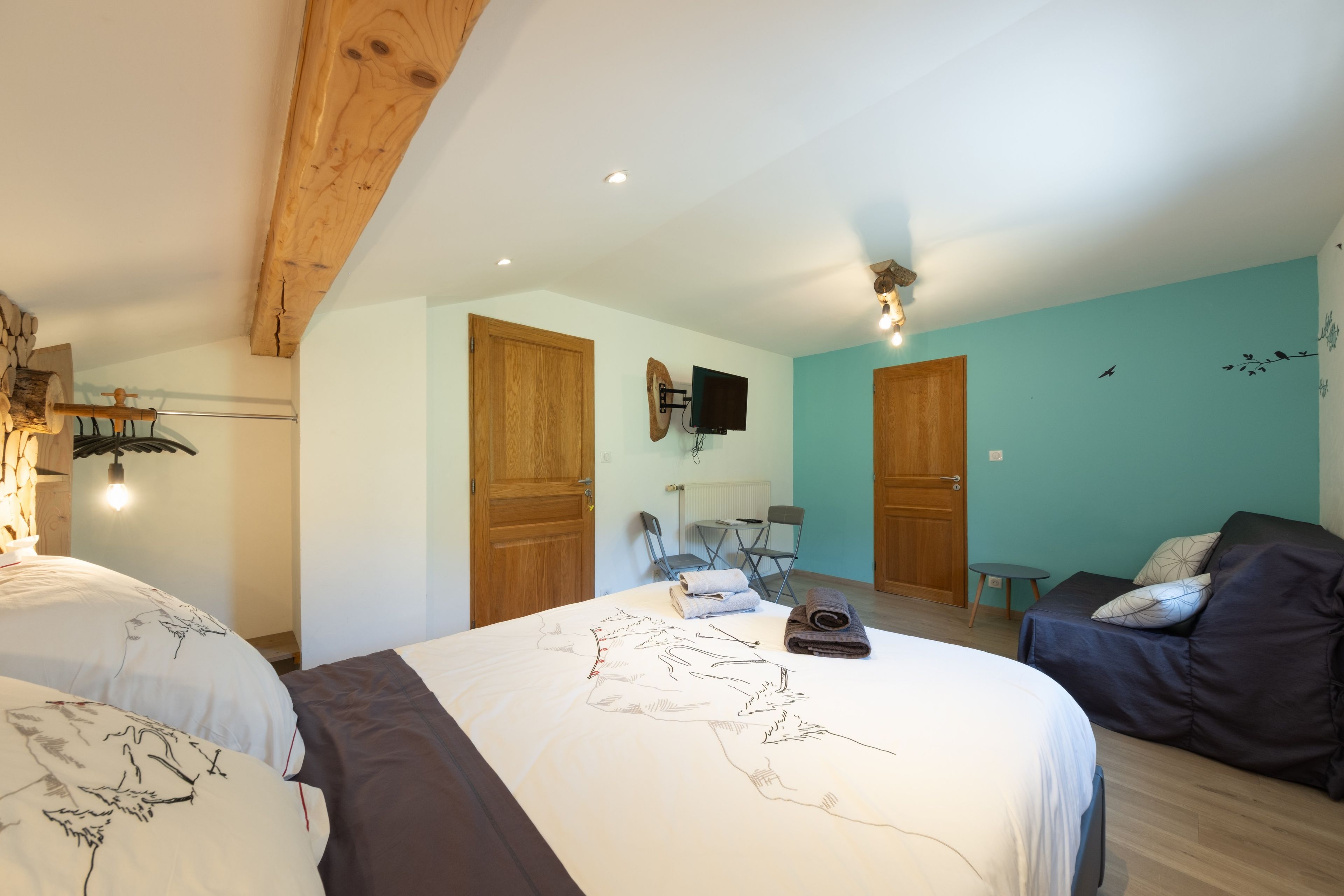 Ein Schlafzimmer mit zwei Betten, einer Holzbalkendecke, einem an der Wand befestigten Fernseher und einer wandfarbenen Türkis.