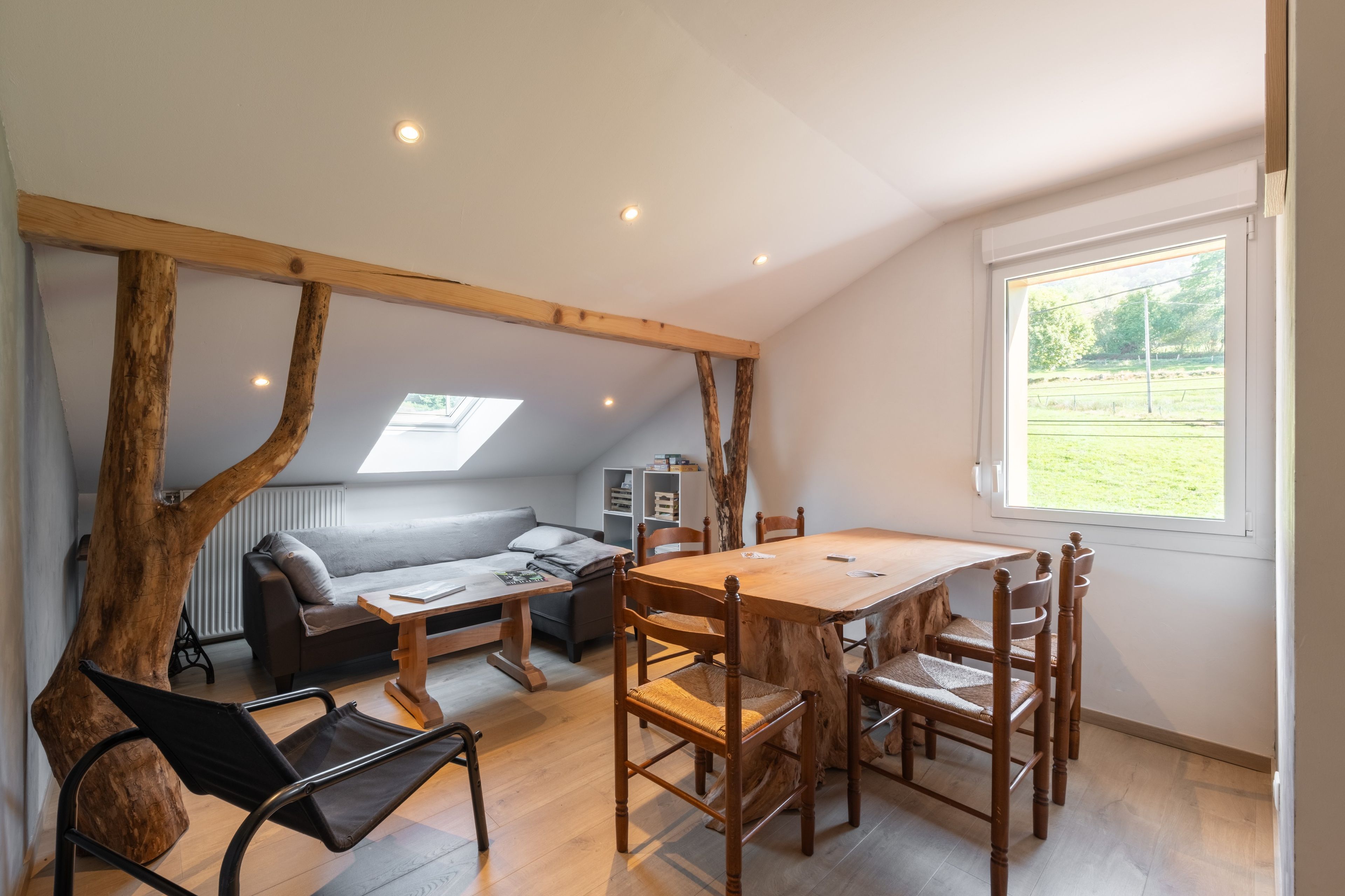 Um quarto acolhedor com uma mesa de jantar de madeira, um sofá e uma janela com vista para um campo gramado.