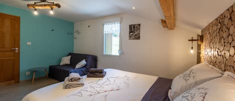 Un dormitorio con una cama, una mesita, una silla, un ventanal y un muro de madera.