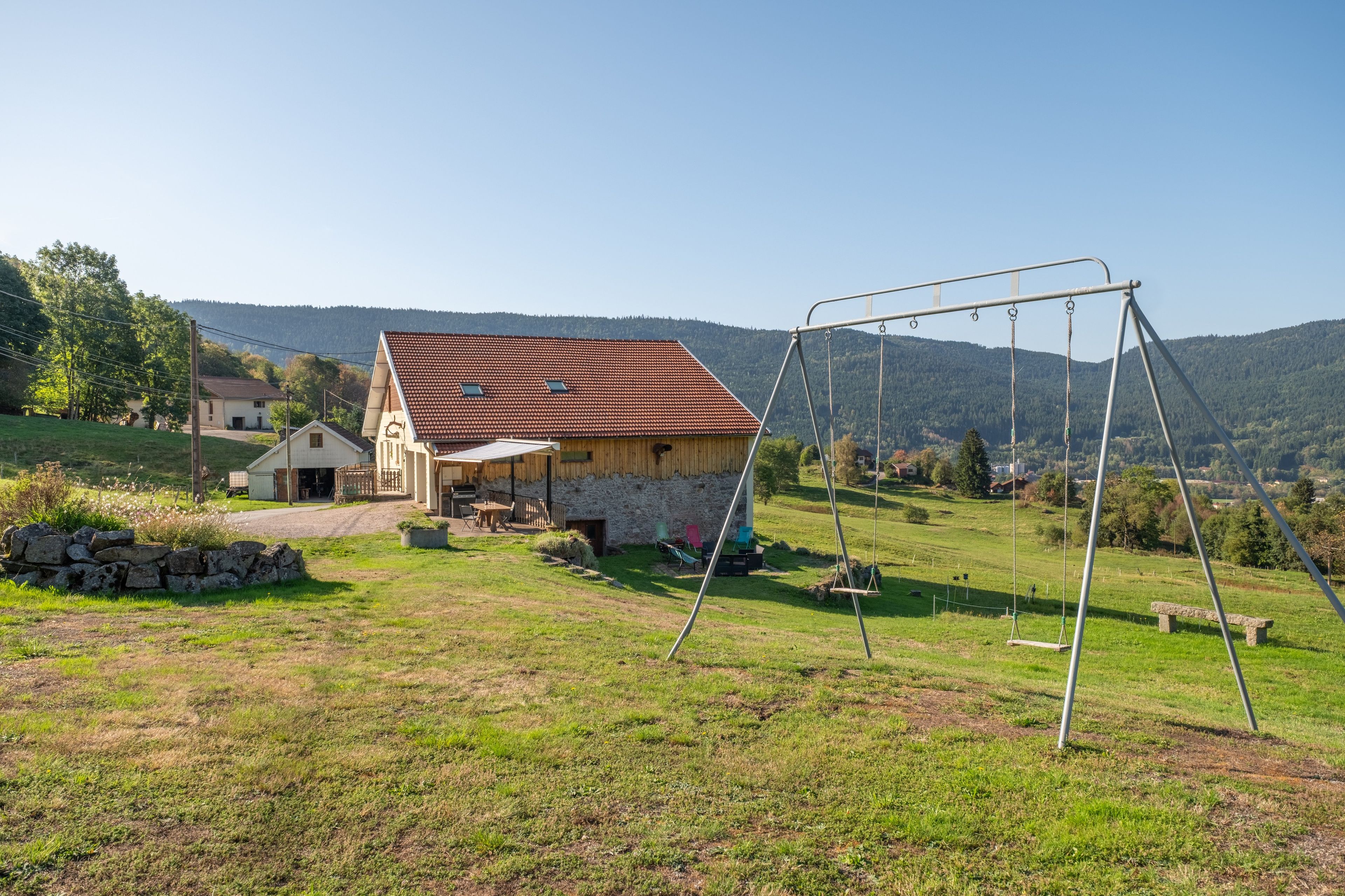 A rural property with a stone house, a swing set, and a view of the surrounding hills.