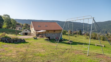 A rural property with a stone house, a swing set, and a view of the surrounding hills.