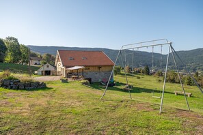 A rural property with a stone house, a swing set, and a view of the surrounding hills.