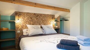 Een slaapkamer met een bed, kussens, een houten hoofdbord, een plank, een kledingroede en een wandlamp.