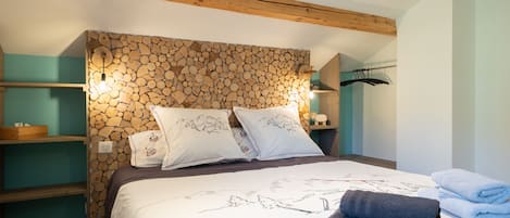 Ein Schlafzimmer mit Bett, Kissen, einem Holzkopfteil, einem Regal, einer Kleiderstange und einer Wandleuchte.