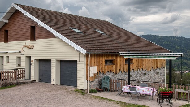 En tvåvåningsbyggnad med ett sluttande tak, ett garage och en täckt uteplats med ett bord och stolar.