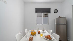 Cocina compacta con una mesa de desayuno dispuesta, un refrigerador y una ventana con persianas.