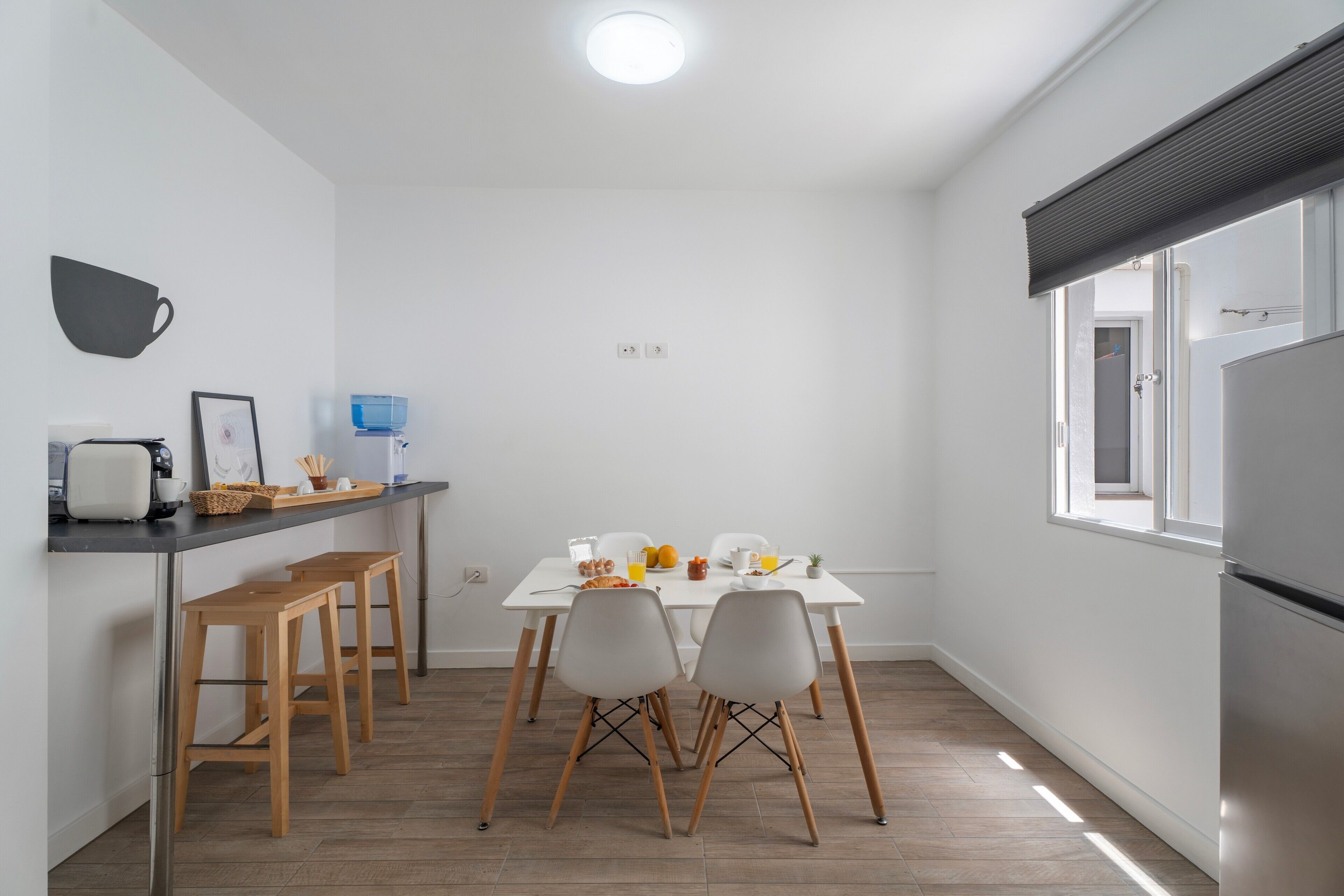 Cocina compacta con mesa, sillas, cafetera y dispensador de agua.