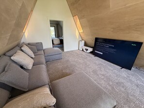 Une chambre de style loft moderne, avec un canapé d’angle, un téléviseur à écran plat et une porte visible donnant sur une autre pièce.