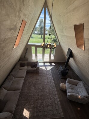 Une chambre à coucher confortable, aménagée en style «loft», avec une grande fenêtre, un lustre, un canapé et un aspirateur.