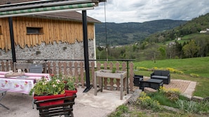 Un bâtiment rustique en bois, doté d’un mur en pierre, d’un balcon avec des meubles d’extérieur et offrant une vue sur une vallée verdoyante.