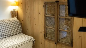 Une pièce avec un mur en bois, une fenêtre donnant sur un champ de foin, une lampe et un canapé à carreaux.