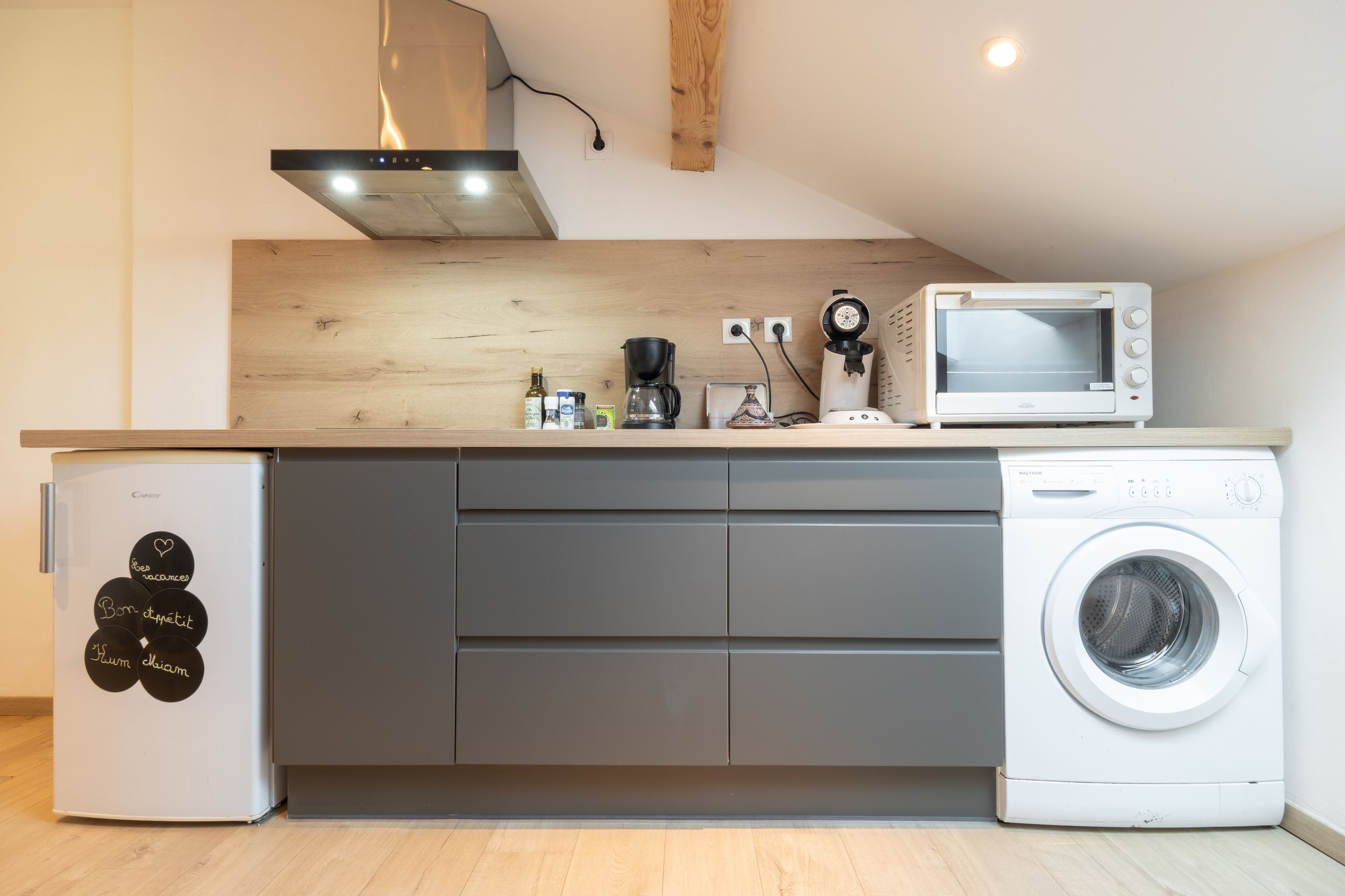 Een kleine keuken met een koelkast, magnetron, koffiezetapparaat en wasmachine.
