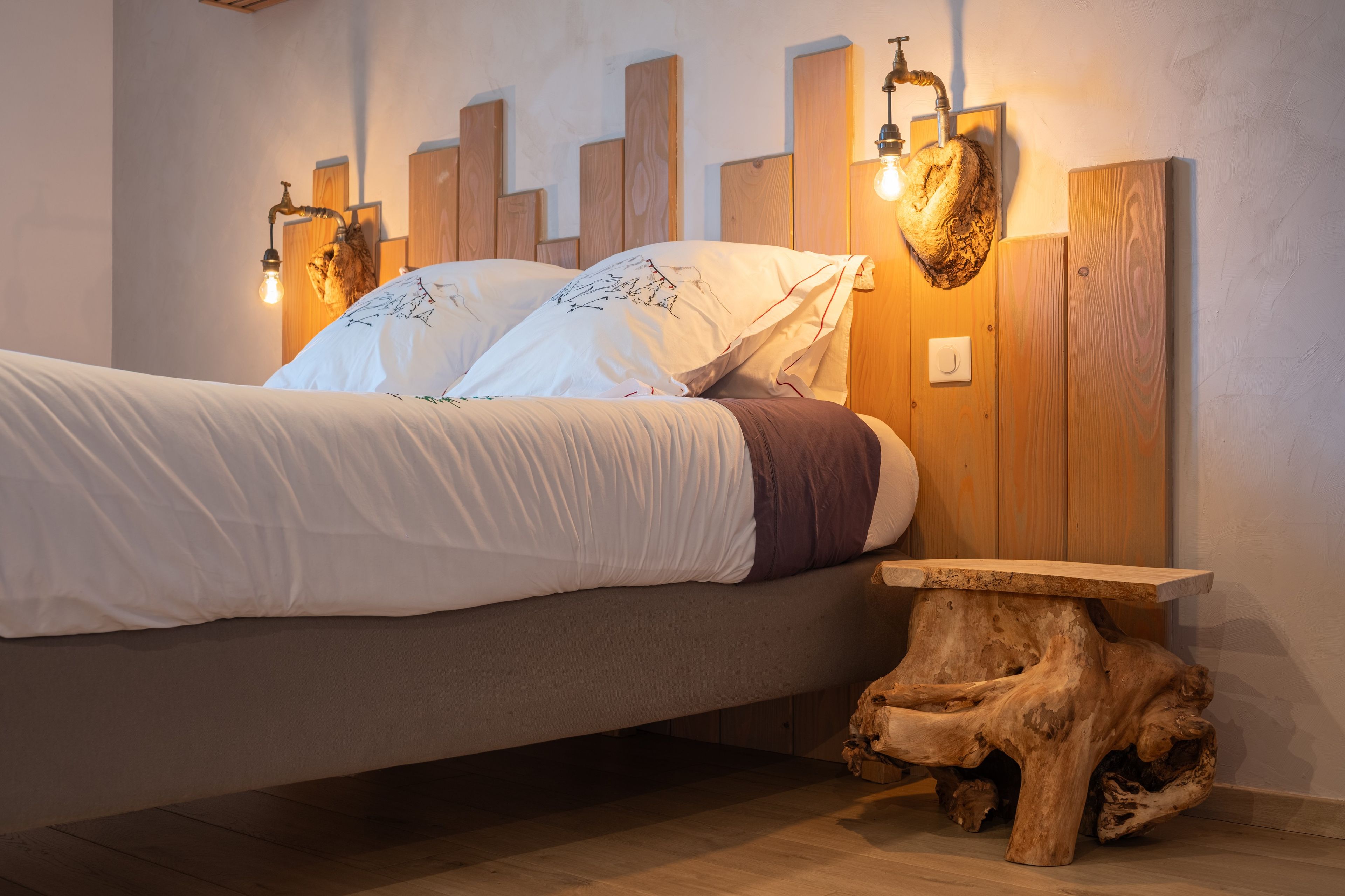 Un lit doté d’une tête de lit ornée de panneaux en bois verticaux et de luminaires fixés au mur.