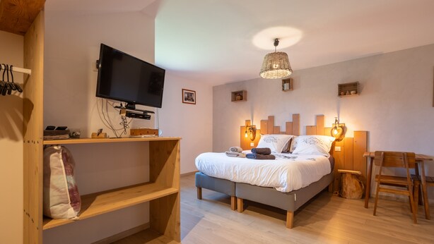 A bedroom with a bed, bedside lamps, a television, a desk, and a chair.