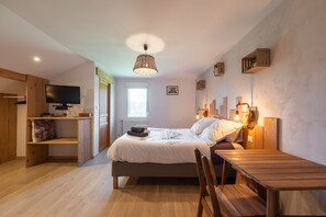 Una camera da letto con un letto, comodino, sedia, televisione e finestra.