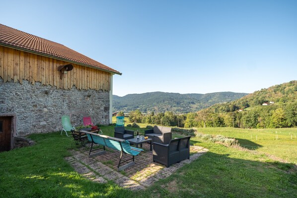A rustic stone building with a tiled roof, a patio area with outdoor furniture, and a scenic view of rolling hills.