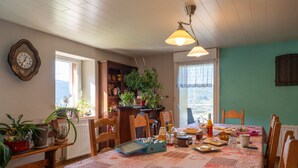 A dining area with a table set for breakfast, chairs, a clock on the wall, and a view through the window.