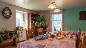 Een eetruimte met een ontbijttafel, stoelen, een klok aan de muur en uitzicht door het raam.