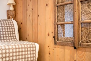 Una pared de madera con una ventana, una cama con colcha escocesa y una lámpara.