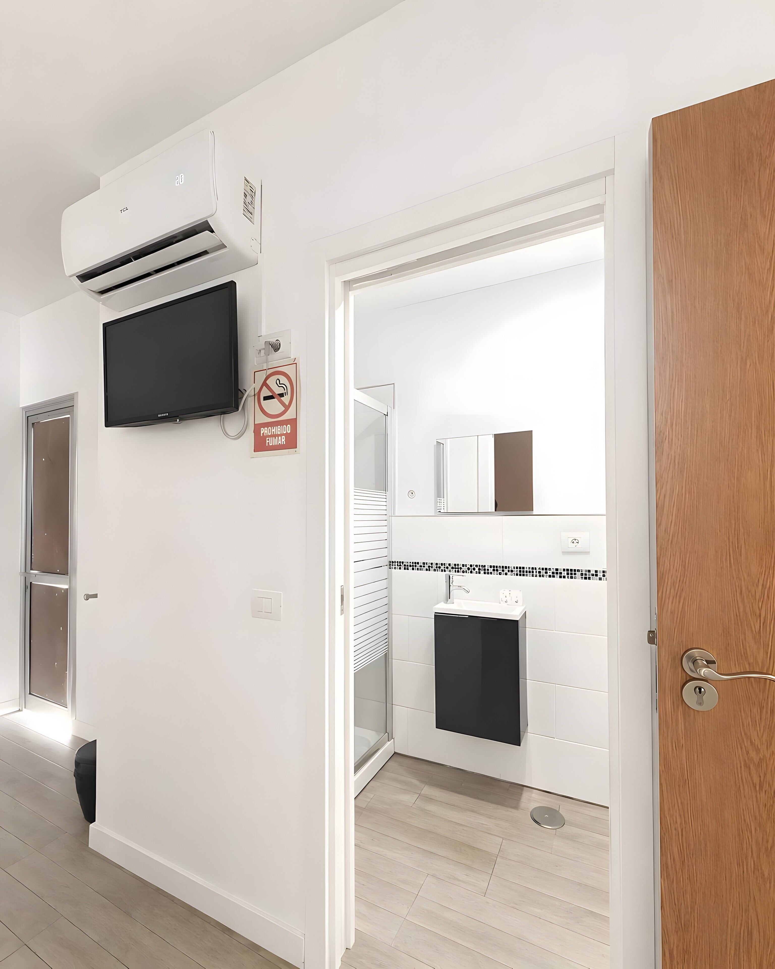 A modern bathroom with a shower, toilet, and sink, a mounted TV, and an air conditioning unit.
