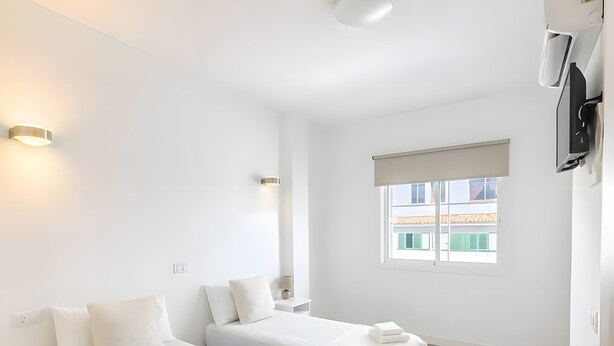 Habitación de hotel con dos camas, ventana con vistas, mesita de noche con lámpara y puerta con manija.