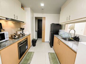 A compact kitchen with a microwave, stove, refrigerator, and sink. - 2BR Uptown Condo BGC-22Floor view and near Mitsukoshi & Uptown Mall, Restaurants (Makati City)