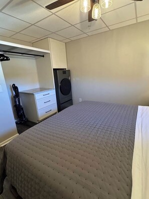 Un dormitorio con cama, lavadora, armario y aspiradora.