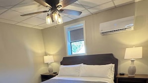A bedroom with a bed, two bedside tables, a ceiling fan, an air conditioning unit, and a window.
