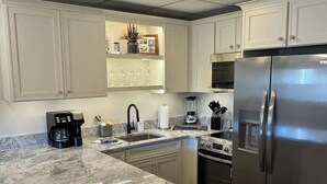A kitchen with white cabinets, a stainless steel refrigerator, a built-in oven, and a granite countertop.