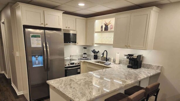 A kitchen with a stainless steel refrigerator, a built-in oven, a sink, and a marble countertop.