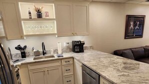 A kitchen with a marble countertop, wooden flooring, and a dishwasher.