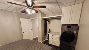 Un dormitorio con cama, ventilador de techo, lavadora y armario.