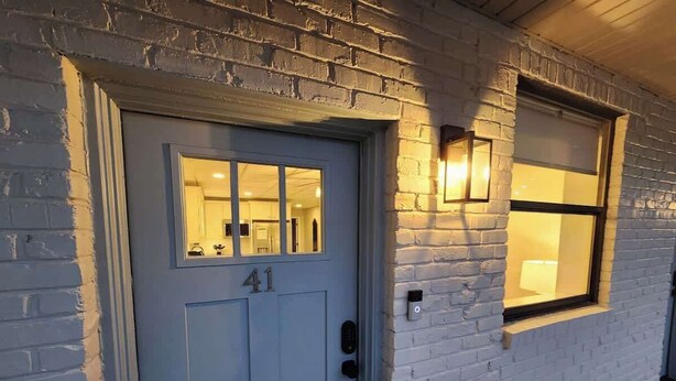 Una casa con una puerta azul marcada con el número 41, una ventana con una lámpara y una pequeña luz exterior en la pared.