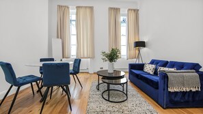 Ein modernes Wohnzimmer mit einem blauen Sofa, passenden Sesseln, einem runden Couchtisch und einer Stehlampe.