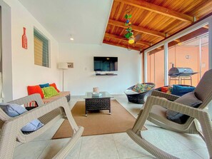 A living room with wicker furniture, a flat-screen TV, and a ceiling fan. - Casa Familiar de Playa, Condominio Malaga Bejuco (Parrita)