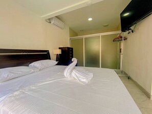 A hotel room with a bed, a TV, an air conditioning unit, a wardrobe, and a shoe rack. - Casa Familiar de Playa, Condominio Malaga Bejuco (Parrita)
