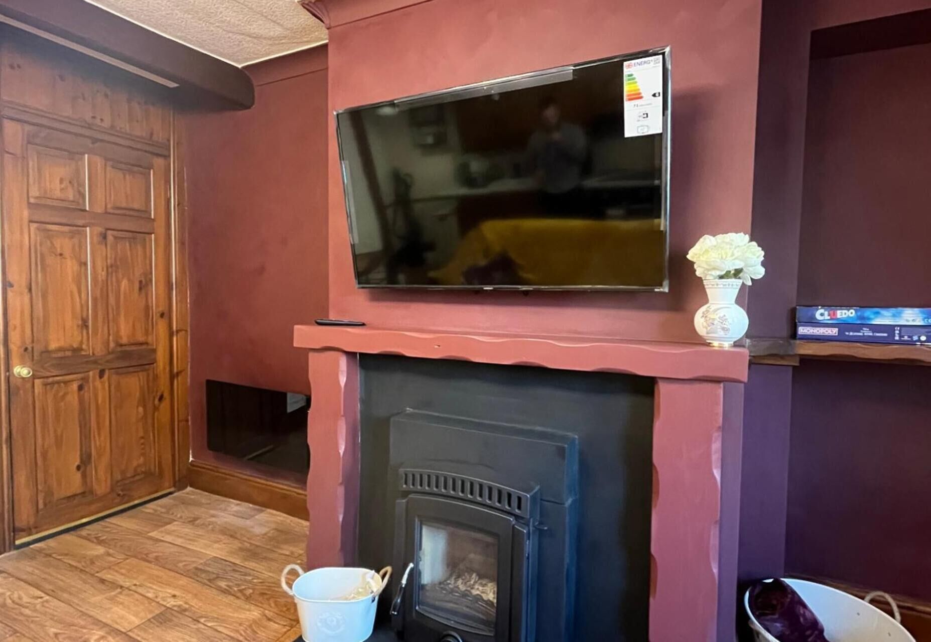 Een woonkamer met een open haard, een tv aan de muur en een bloevas.