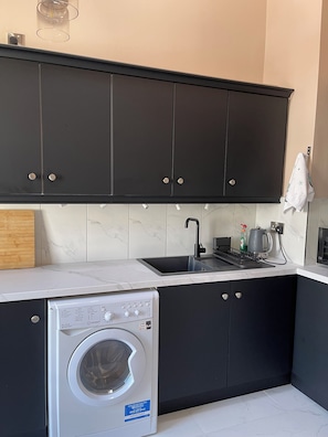A compact kitchen with a built-in washer, dark cabinets, and a white countertop. - Apartment 54, Castle Gate is a spacious top-floor apartment in the heart of Dub (Dublin)